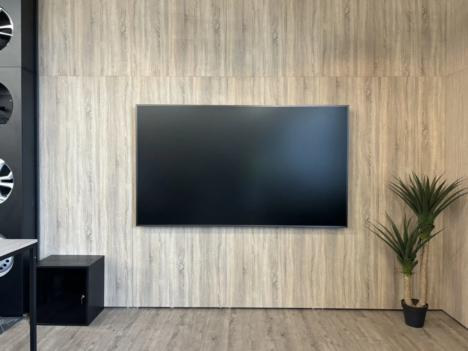 Salle de réunion ou de vie d'entreprise moderne équipée d'un système audiovisuel intégré professionnel : murs épurés, large écran de vidéoconférence haute définition intégré, système sonore discret, câblage et technologies de pointe invisibles ou élégamment intégrés, mobilier professionnel contemporain. L'image doit mettre en évidence le caractère « sur mesure » et haute technologie de l'installation, montrant une solution audiovisuelle sophistiquée et connectée adaptée à une entreprise moderne.